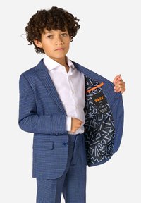 Giacca in ajustar houndstooth blu con camicia bianca. La fodera interna presenta motivi astratti in bianco e nero con un accento arancione.
