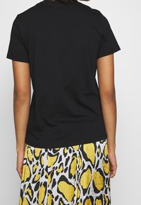 Černé bavlněné tričko s klasickým střihem a krátkými rukávy, doplněné vzorovanou žluto-bílou sukní s černými akcenty.