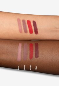 Quattro campioni di rossetto in diverse tonalità: rosa chiaro, mauve, rosso e bordeaux profondo su un braccio chiaro, abbinati a quattro tonalità simili su un braccio scuro.