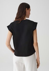 Zwart top met korte, gestructureerde mouwen. Het voorpand is glad, met een gebogen zoom. Gemaakt in combinatie met witte, ruime broek.