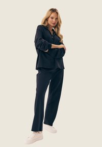 Czarny oversize sweter z kołnierzem na zamek, w połączeniu z dopasowanymi szerokimi spodniami. Białe trampki dopełniają stylizację, podkreślając swobodny wygląd.