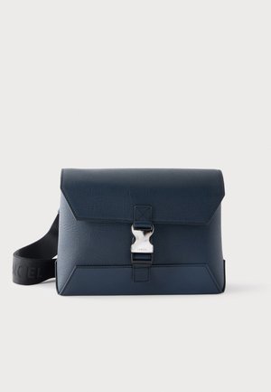 Sac bandoulière en cuir bleu foncé avec une bandoulière noire réglable et une fermeture argentée à l'avant sur un fond uni.