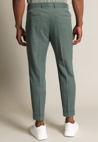 Miętowo-zielone, dopasowane spodnie z tylnymi kieszeniami, zwężane i podwinięte nogawki, zestawione z białymi trampkami. Teksturowana tkanina i czyste linie.