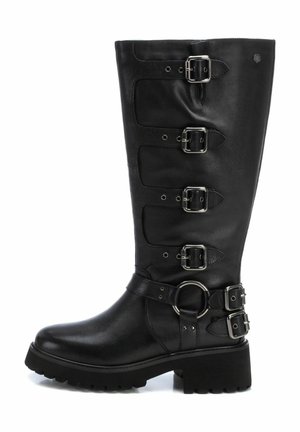 Bota de cuero negro hasta la rodilla con cinco hebillas plateadas, un acento circular cerca del tobillo y una suela de goma texturizada. Diseño de tacón plano.