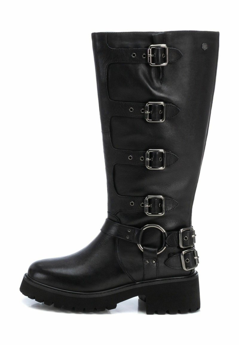 Bota de cuero negro hasta la rodilla con cinco hebillas plateadas, un acento circular cerca del tobillo y una suela de goma texturizada. Diseño de tacón plano.
