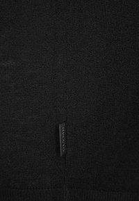 Schwarzer Strickpullover mit feiner Textur. Enthält ein kleines Etikett mit dem Markennamen am Saum. Schlichtes und minimalistisches Design.