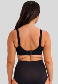 Sostenedor negro con tirantes ajustables, diseño sin costuras y cierre de gancho y ojo en la parte de atrás. El material parece suave y elástico.