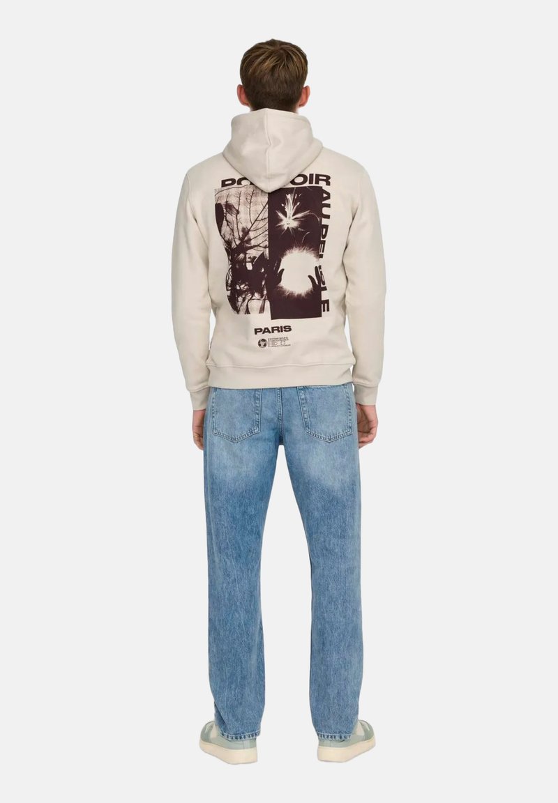 Sudadera crema con un estampado gráfico en la parte posterior que presenta diseños abstractos. Combinada con jeans de denim azul claro y zapatillas blancas.