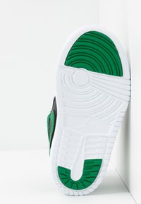 Semelle de sneakers noire et verte, avec une semelle intermédiaire en caoutchouc blanc texturé, un motif de tread circulaire et des accents verts proéminents.