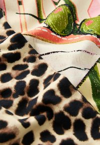 Textiles featuring a pink and green botanical print alongside a beige fabric with a black and brown leopard pattern. Soft texture, vibrant colors.