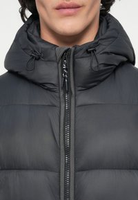 Chaqueta de plumas negra con cuello alto, cremallera frontal con un tirador texturizado y cordones ajustables en la capucha para un ajuste ceñido.