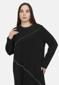 Schwarzes Langarmkleid mit goldenen diagonalen Nähten, aus weichem Stoff gefertigt, mit rundem Halsausschnitt und entspannter Silhouette.