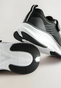 Baskets de sport noires avec une tige en mesh texturé et une semelle en caoutchouc blanche. Œillet de traction à l'arrière et design à rayures contrastées sur le côté.