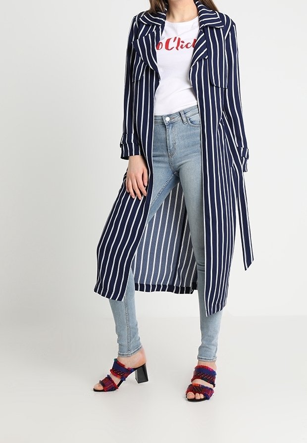 Dlouhý kabát s námořnickými modrými a bílými pruhy s límečkem, doplněný bílým tričkem s červeným nápisem, světle modrými džíny a vícebarevnými sandály na podpatku.
