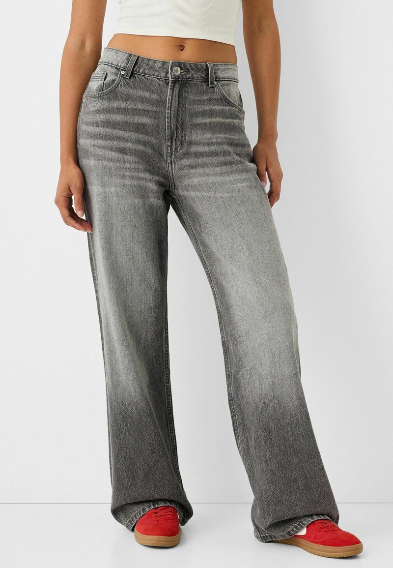 Grå vida jeans med en urtvättad finish, med knappstängning och design med fem fickor. Matchas med röda skor, vilket ger en avslappnad look.