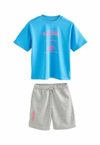 Blå bomulds t-shirt med pink grafik, parret med grå bomulds shorts med pink tekst på benet. Begge items har en afslappet pasform.