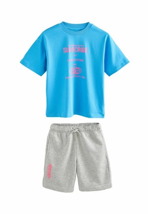 Tricou din bumbac albastru cu grafica roz, asortat cu șorturi din bumbac gri care au text roz pe picior. Ambele articole au o croială lejeră.
