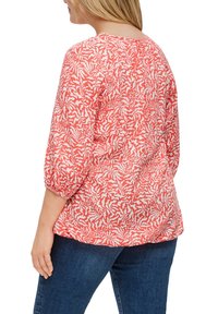 Blouse à motifs rouges et blancs avec des manches trois-quarts, un col froncé et une coupe décontractée, associée à un jean foncé.