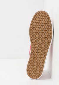 Kumipohjallinen, jossa on kuusikulmainen kuvio, vaaleanruskea pohja ja valkoiset reunat, nähtynä pohjasta valkoista taustaa vasten.