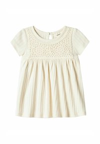 Haut à manches courtes crème clair avec un corsage en crochet texturé et une jupe plissée. Le dos présente une ouverture en forme de clé avec une fermeture à bouton.