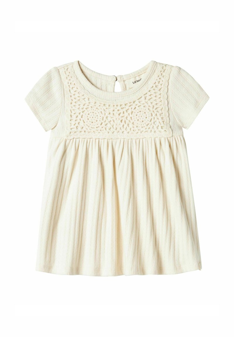 Haut à manches courtes crème clair avec un corsage en crochet texturé et une jupe plissée. Le dos présente une ouverture en forme de clé avec une fermeture à bouton.