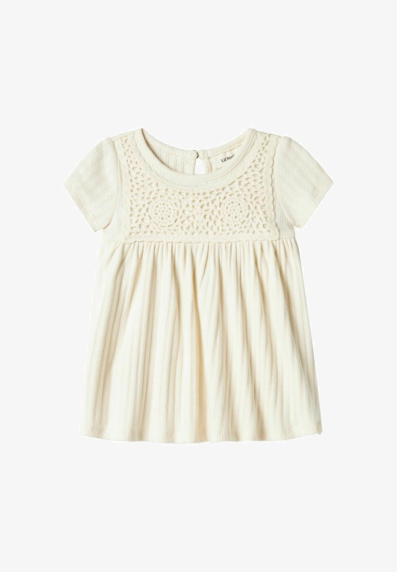 Jasna kremowa bluzka z krótkim rękawem, z koronkowym, teksturowanym przodem i plisowanym dołem. Tył ma otwarcie w kształcie łezki z zapięciem na guzik.