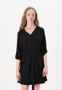 Schwarzes knielanges Kleid aus einem glatten Stoff, mit V-Ausschnitt, drei Viertelärmeln und einem passenden Stoffgürtel an der Taille.