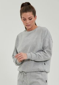 Grå sweatshirt av mjukt tyg med rund halsringning, avslappnad passform, ribbade ärmslut och elastisk nederkant. Har sidoflaggor.