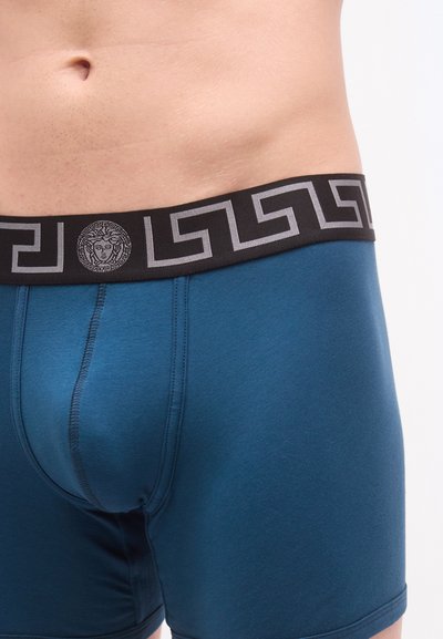 Ανδρικά μποξεράκια σε τιρκουάζ ύφασμα, με μαύρη ζώνη μέσης που έχει γκρι ελληνικό σχέδιο και στρογγυλό λογότυπο στο κέντρο. Λείο υφή.