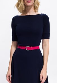 Marineblaues Kleid mit kurzen Ärmeln und einem U-Boot-Ausschnitt, in der Taille mit einem leuchtend pinken Leder Gürtel mit einer runden silbernen Schnalle tailliert.