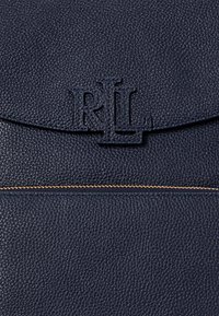 Σκούρο μπλε δερμάτινη τσάντα χειρός με υφή, ανάγλυφο λογότυπο "RL" και χρυσή λεπτομέρεια στον φερμουάρ κατά μήκος της κάτω ραφής.