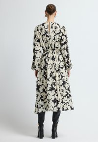 Vestido con estampado floral en negro y crema, de manga larga, con cintura ceñida, detalle de abertura en la espalda y terminando a media pantorrilla, combinado con botas de tacón negras.