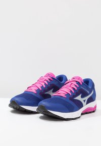 Des chaussures de sport bleues avec des lacets roses, une tige en maille et une semelle en caoutchouc noire, présentant un détail de logo argenté sur le côté.