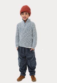 Maglione lavorato a maglia azzurro chiaro con colletto a mezza zip, abbinato a pantaloni cargo in velluto a coste blu scuro e scarpe stringate marroni. Beanie lavorato a maglia rosso.