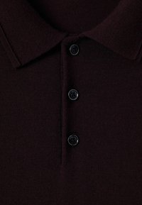 Polo di colore bordeaux realizzato in tessuto a maglia testurizzato, con colletto classico e quattro bottoni neri sul davanti.