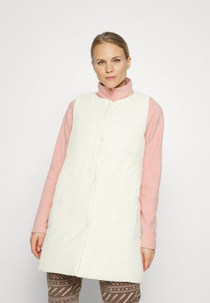 Colete acolchoado branco com gola alta, apresentando botões de pressão e bolsos laterais, usado sobre uma blusa de manga longa rosa e leggings estampadas.