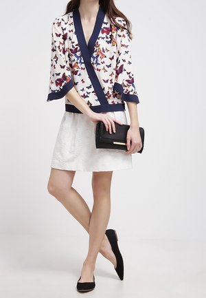 Top estilo kimono con estampado de mariposas en blanco, acentos en azul marino y mangas de tres cuartos, combinado con una falda blanca texturizada y un clutch negro.