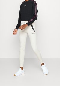 Zwarte cropped sweatshirt met roze streepdetails, gecombineerd met crème joggers met ritszakken en een logo, compleet met witte sneakers.