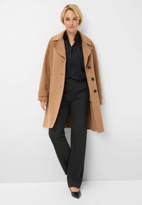 Tan wollen mix jas met grote knopen en een notch-kraag, gecombineerd met donkere pantalons met streepjes en zwarte schoenen. Eenvoudig, op maat gemaakt ontwerp.