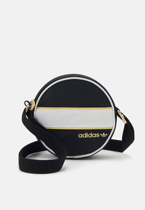 Ronde zwarte Adidas crossbodytas met witte en gouden horizontale streep, gouden logo en verstelbare zwarte stoffen schouderriem.