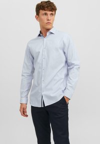 Cămașă button-up de culoare albastru deschis, cu o textură subtilă, mâneci lungi, guler ascuțit și nasturi albi. Asortată cu pantaloni negri.