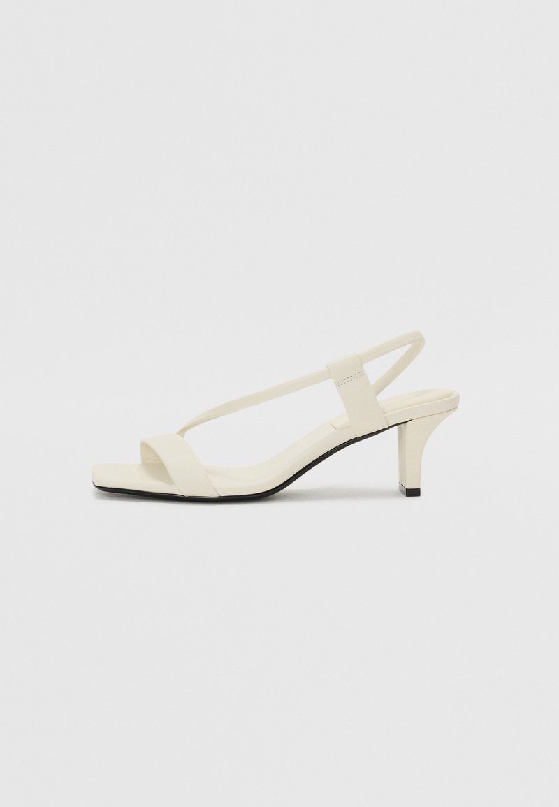 Beige block-heeled sandals with thin straps and a square toe. Smooth material with minimal detailing, designed for easy wear.
