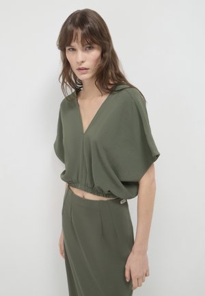 Top corto verde oliva con scollatura a V profonda e orlo elastico, abbinato a una gonna coordinata. Tessuto leggero con una consistenza liscia.