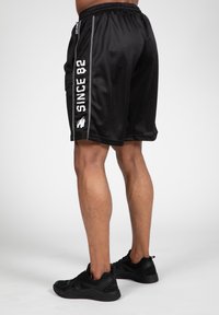 Zwarte sportshorts van meshstof met een elastische tailleband, voorzien van een witte tekst "SINCE 82" langs de zijkant.