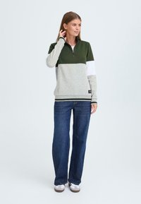 Fleece pullover met een halve ritssluiting in groen, grijs en wit; voorzien van geribbelde mouwen en zoom. Geldig met wijde blauwe jeans en casual schoenen.