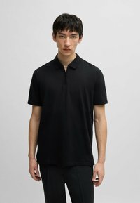 Polo nero con collo zip, maniche corte e una vestibilità comoda. Realizzato in tessuto liscio con un design semplice e pulito.