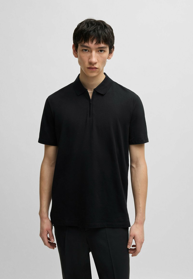 Polo nero con collo zip, maniche corte e una vestibilità comoda. Realizzato in tessuto liscio con un design semplice e pulito.
