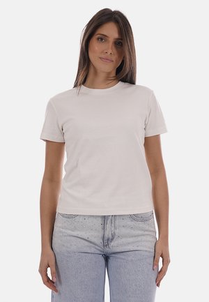 Donna con capelli castani lisci che indossa una semplice t-shirt bianca a maniche corte e jeans a vita alta azzurri con dettagli in strass.