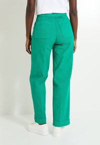 Pantalones verdes de talle alto con un corte relajado, que cuentan con dos bolsillos traseros y bajos remangados, fabricados en una tela suave y ligera.