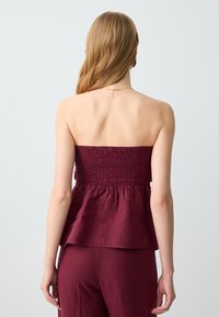 Top bordeaux senza spalline con corpino smock e orlo a peplo, realizzato in tessuto leggero. Texture liscia con una vestibilità comoda.